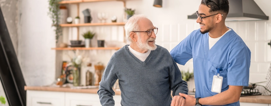 Life Assure Medical Worker Helping His Patient Move Around Apartment Hero